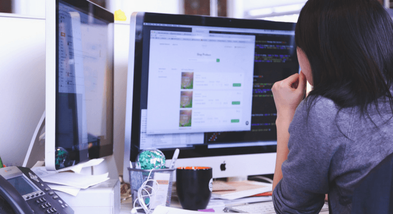 Woman faces her desktop computer while sitting at a work station