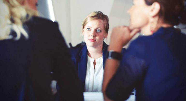 Three women sitting in a meeting. One facing the camera. 