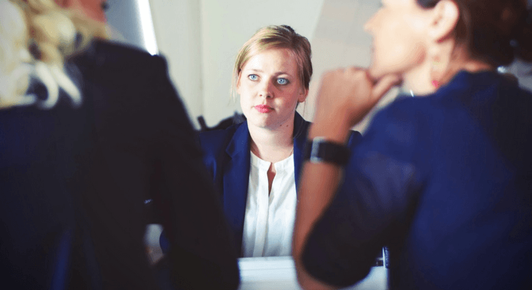 Group of three women sitting at a table. One faces the camera. 