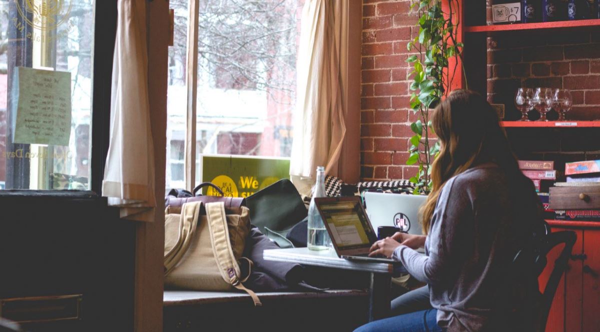Woman in front of a cafe window typing on a laptop 