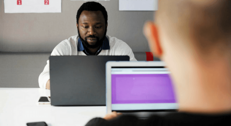 Man in a classroom sitting at a table with a laptop