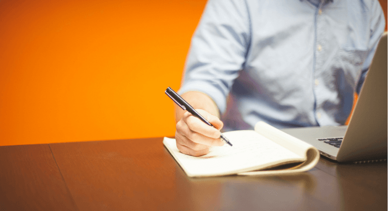 Man researching on a laptop and taking notes 