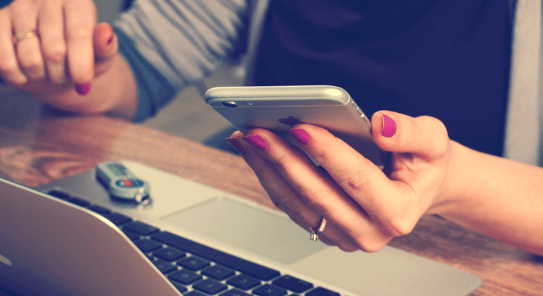 Close up of woman holding a call phone while a laptop sits in the foreground