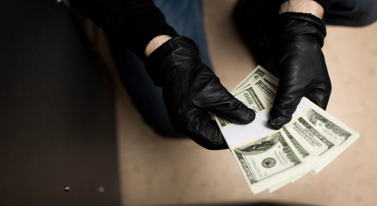 Black gloved hands hold bundles of hundred dollar bills as if to steal 