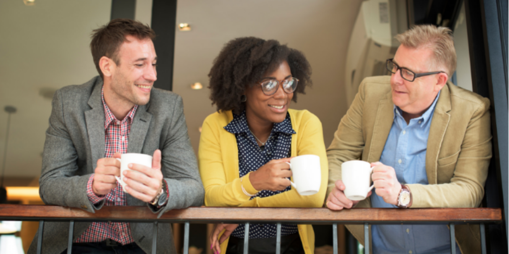 Employees, two men and a women, talking and drinking coffee while leaning on a railing